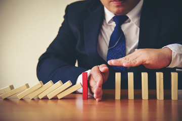 Businesswoman Hand Stopping Dominoes From Falling On Office Desk. Risk Prevention Concept