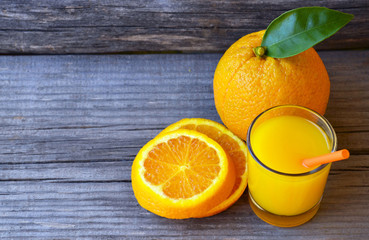 Glass of fresh orange juice,ripe orange fruit and slices on rustic wooden table.Freshly squeezed orange juice with drinking straw,orange fruit and orange slices.Selective focus.