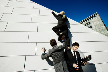 2 men helping woman over wall