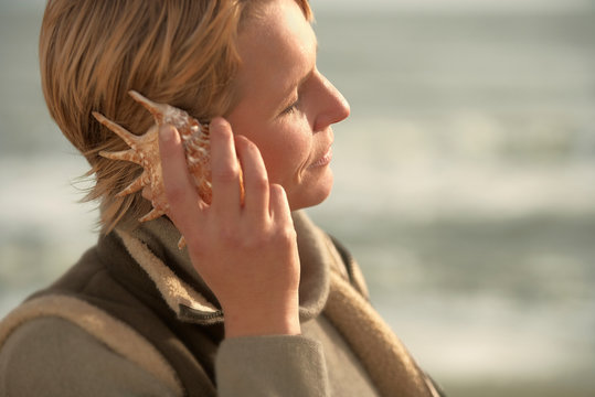 Woman by sea, listening in seashell