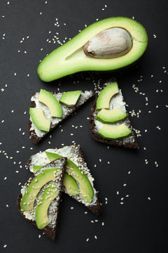 Dietary sandwiches with fresh organic sliced avocado and cream cheese top on a black background, vertically.