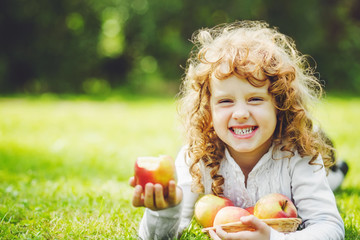 Little girl is eating apple and smiling showing white teeth.