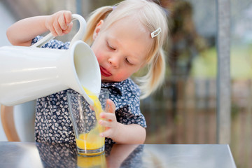 Toddler girl pouring glass of juice