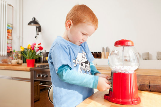 Boy using gum ball machine in kitchen