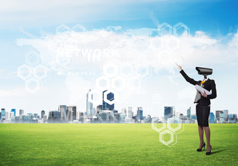 Camera headed woman standing on green grass against modern cityscape