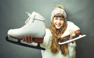 A girl with skates in her hands in a white sweater and hat. - obrazy, fototapety, plakaty