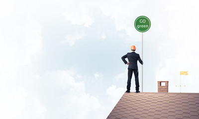 Businessman in suit on house top with ecology concept signboard.