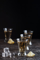 Strong whiskey in glasses with ice and sliced lemon on the dark background