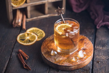 Cocktail with iced tea, whiskey, orange and ice in a glass on the wooden tray on the dark background