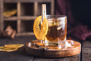 Cocktail with iced tea, whiskey, orange and ice in a glass on the wooden tray on the dark background