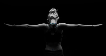 Beautiful fit and healthy blond woman in black top in dark with arms stretched from behind artistic conversion