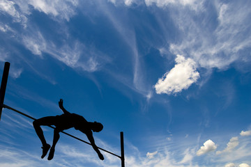 Silhouette of athlete competing in pole vault under the blue sky