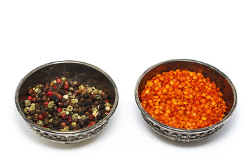 Pepper grains are red, black, white spices, float in a silver bowl. View from above. Isolated on white background.
