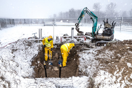 Construction workers working outside in the snow repairing a damaged water pipe