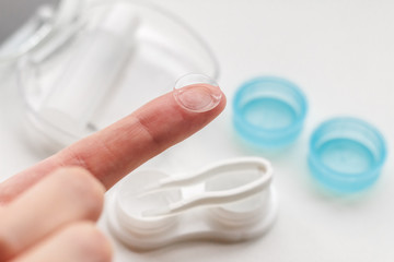 Contact lens on finger on the background of container for storage of lenses