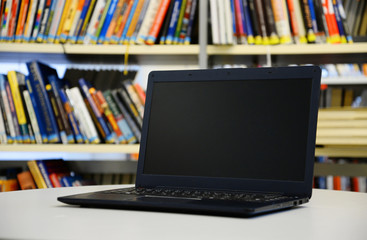 Study in the library. Close up of computer on the table, blurred books in the background. Education concept. Online versus offline study.