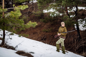 Female hunter in camouflage clothes ready to hunt, holding gun and walking in forest.