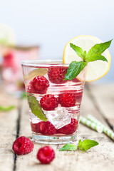 Raspberry lemonade with lemon, mint and ice in the party glass on the wooden background