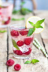 Raspberry lemonade with lemon, mint and ice in the party glass on the wooden background