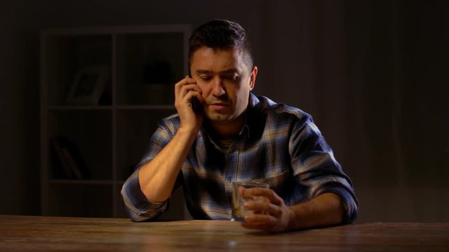 man drinking whiskey and calling on smartphone