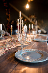 View at decorated table for Christmas eve  in big house with black walls and stylish loft interior. Plates, glasses, many candles and lights under table on roof. Marry Christmas and happy New year.
