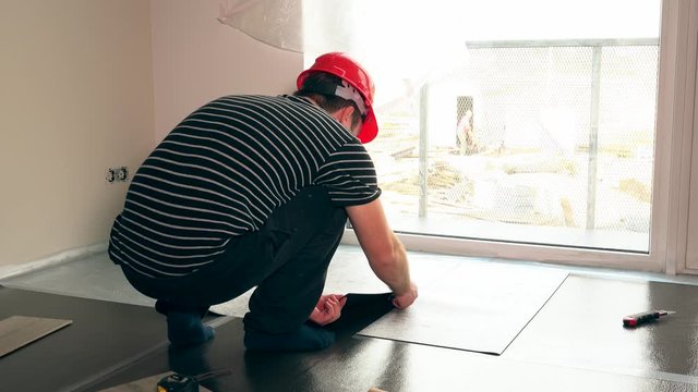 Worker man with scissors cutting teflon underlay mat on floor