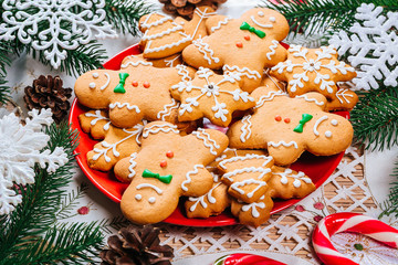 Christmas gingerbread cookies homemade on red plate with branches of Christmas tree and decor on home New Year table. Merry Christmas postcard