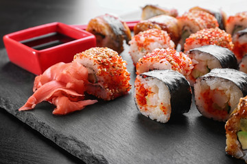 Slate plate with tasty sushi rolls on table