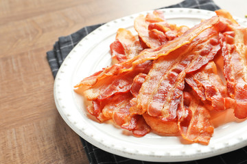 Plate with cooked bacon rashers on table