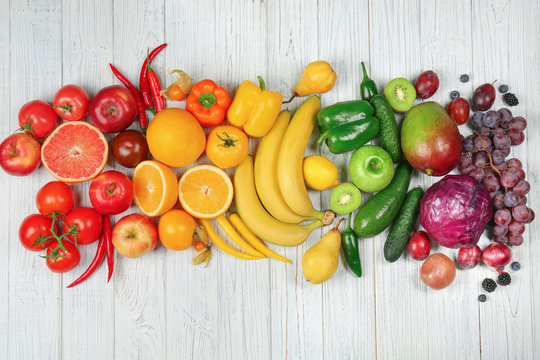 Creative composition made of fruits and vegetables in rainbow colors on wooden background, flat lay