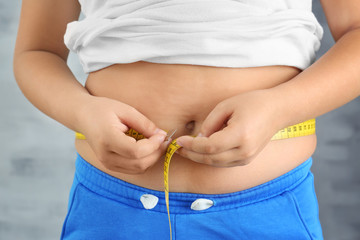 Overweight boy measuring waist on grey background, closeup