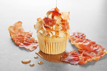 Pouring maple syrup onto cupcake with bacon on table
