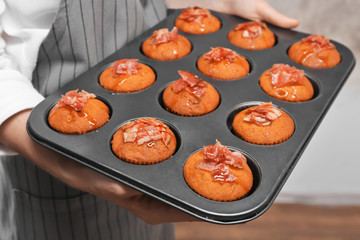 Woman holding baking mold of muffins with bacon, close up