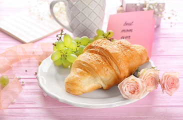 Plate with tasty croissant, grapes and roses on table, closeup