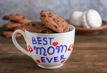 Cup with text BEST MOM EVER and cookies for Mother's day on table