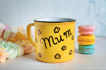 Metal cup with word MUM and sweets for Mother's day on table