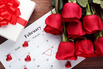 Bouquet of red roses with calendar on february and gift box on wooden table