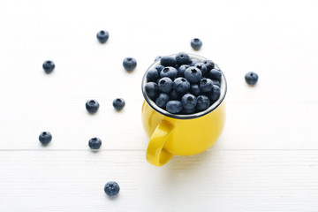 Ripe blueberries in yellow mug on white wooden table