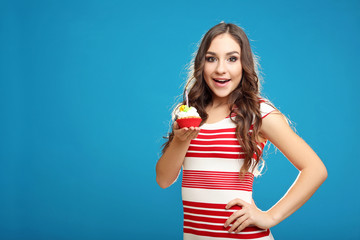 Young woman with cupcake in hand on blue background