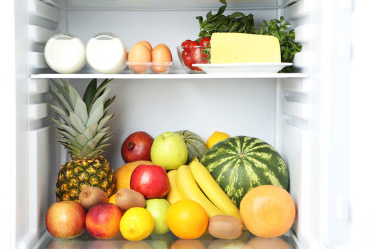 Open fridge full of fruits with cheese and bottle of milk