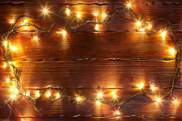 Christmas bokeh background frame. Glowing golden garland on a brown wooden table with branches of Christmas tree.