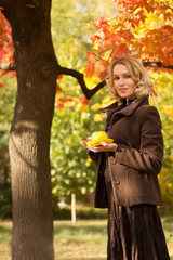 Woman is holding cap under an autumn tree