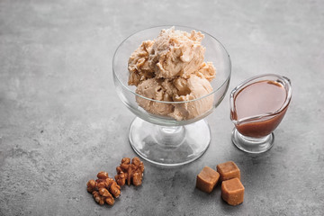 Delicious ice cream and caramel syrup in glassware on grey background