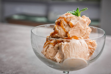 Delicious ice cream with caramel syrup in glass bowl on table