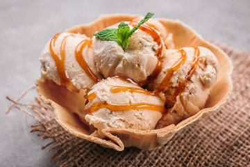 Delicious ice cream with caramel syrup in waffle bowl on table, closeup