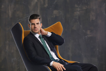 Handsome young man sitting in armchair on dark background