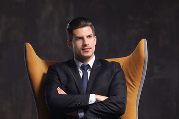 Handsome young man sitting in armchair on dark background