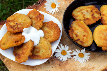 Homemade potato pancakes with sour cream. Potato fritters on white plate on wooden brown background.
