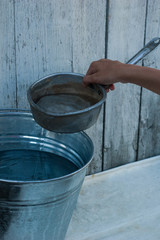 The girl is holding a ladle with water near the bucket.