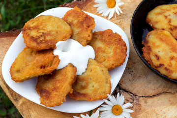 Homemade potato pancakes with sour cream. Potato fritters on white plate on wooden brown background.